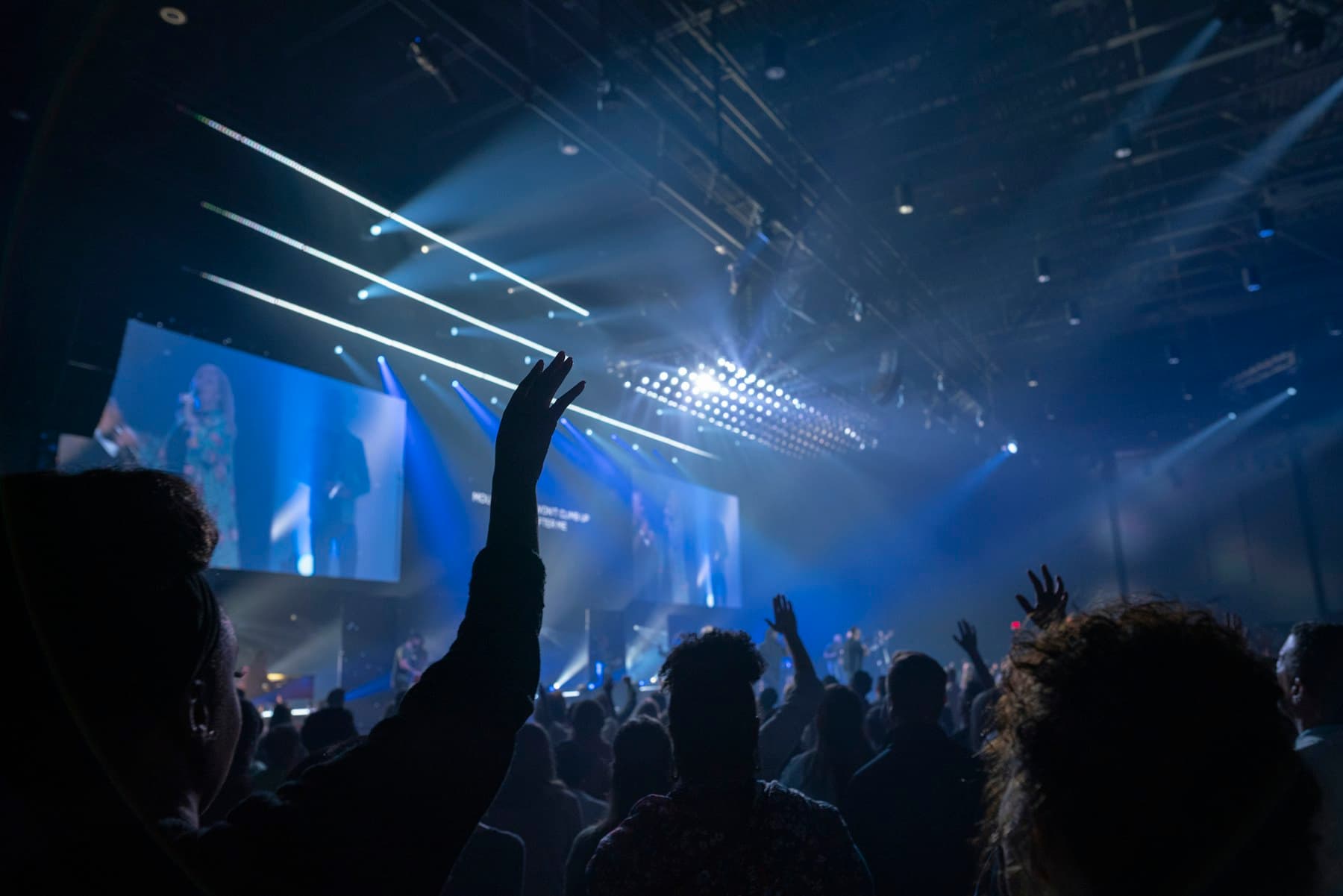 A congregation worshipping beneath blue stage lights